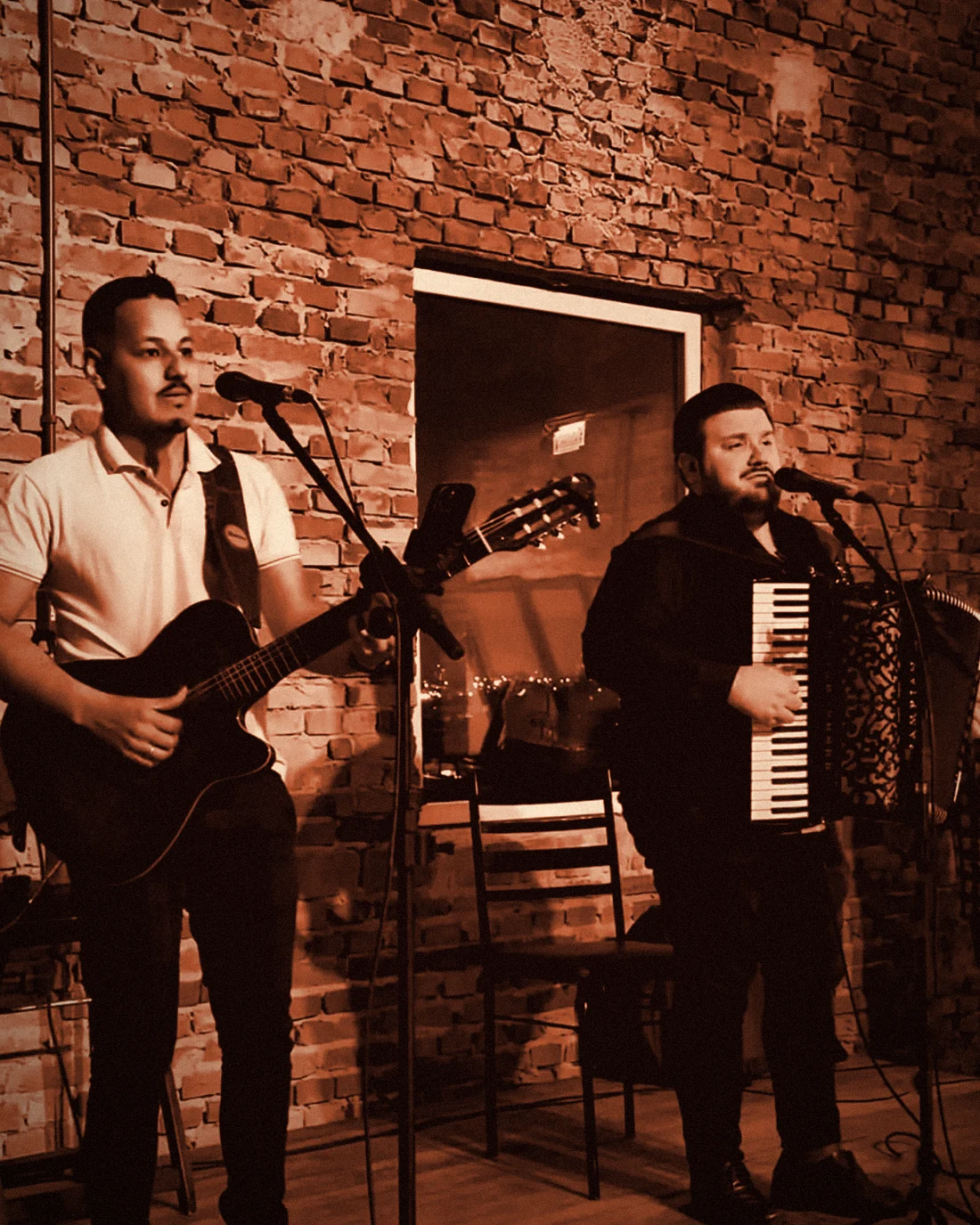 Patrick & Davi tocando ao vivo no formato Acústico, com parede de tijolos ao fundo